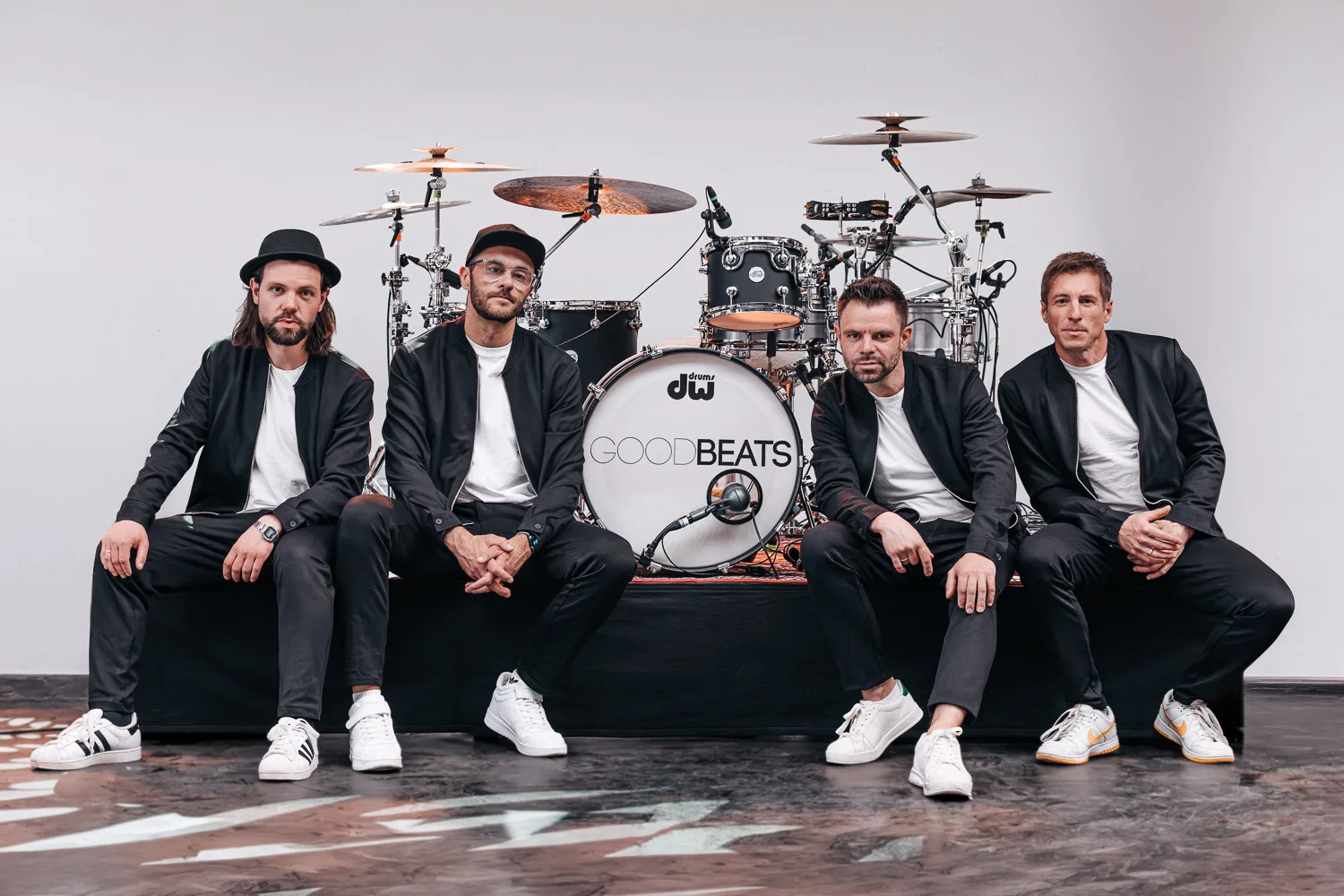 Die vier Musiker der GOODBEATS in schwarzen Jacken und weißen Shirts sitzen vor dem Schlagzeug mit GOODBEATS-Bassdrum